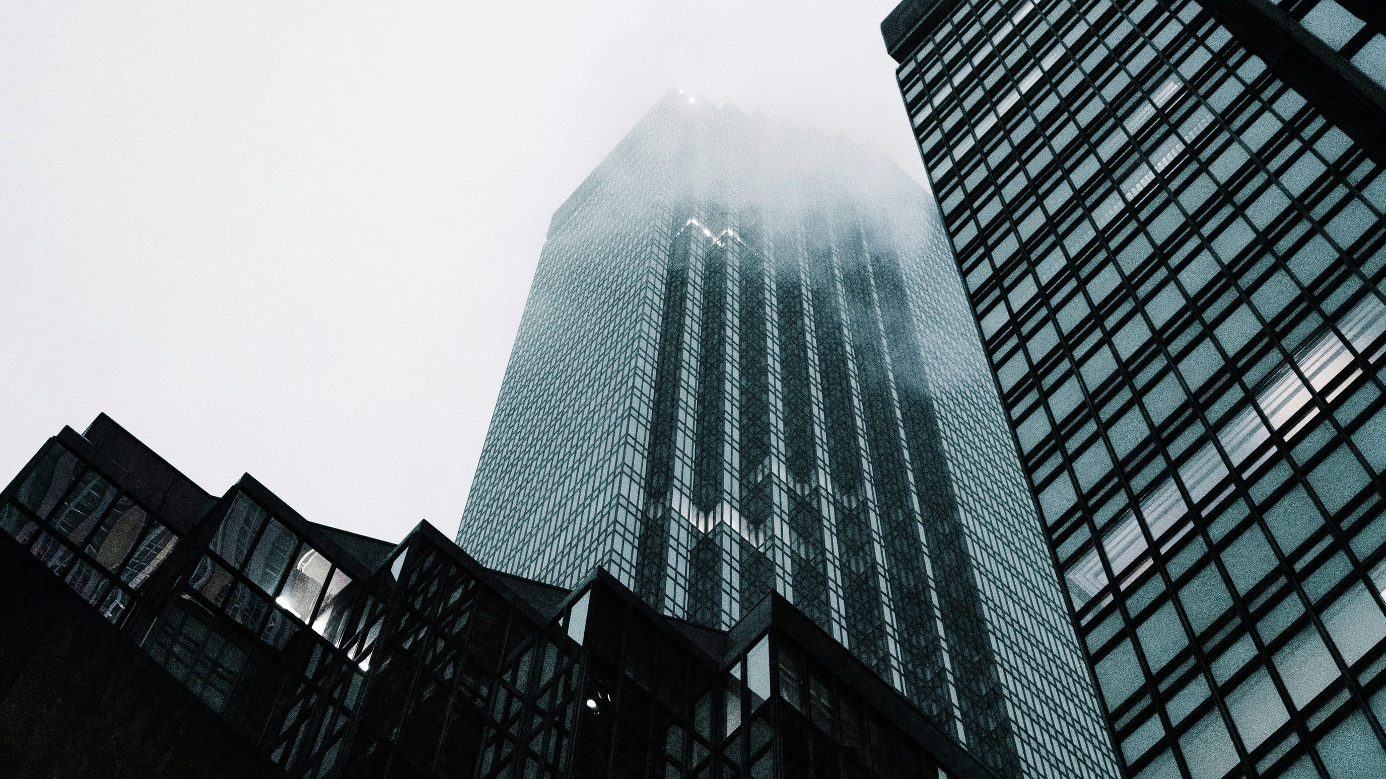 A glass tower rising into fog between dark buildings