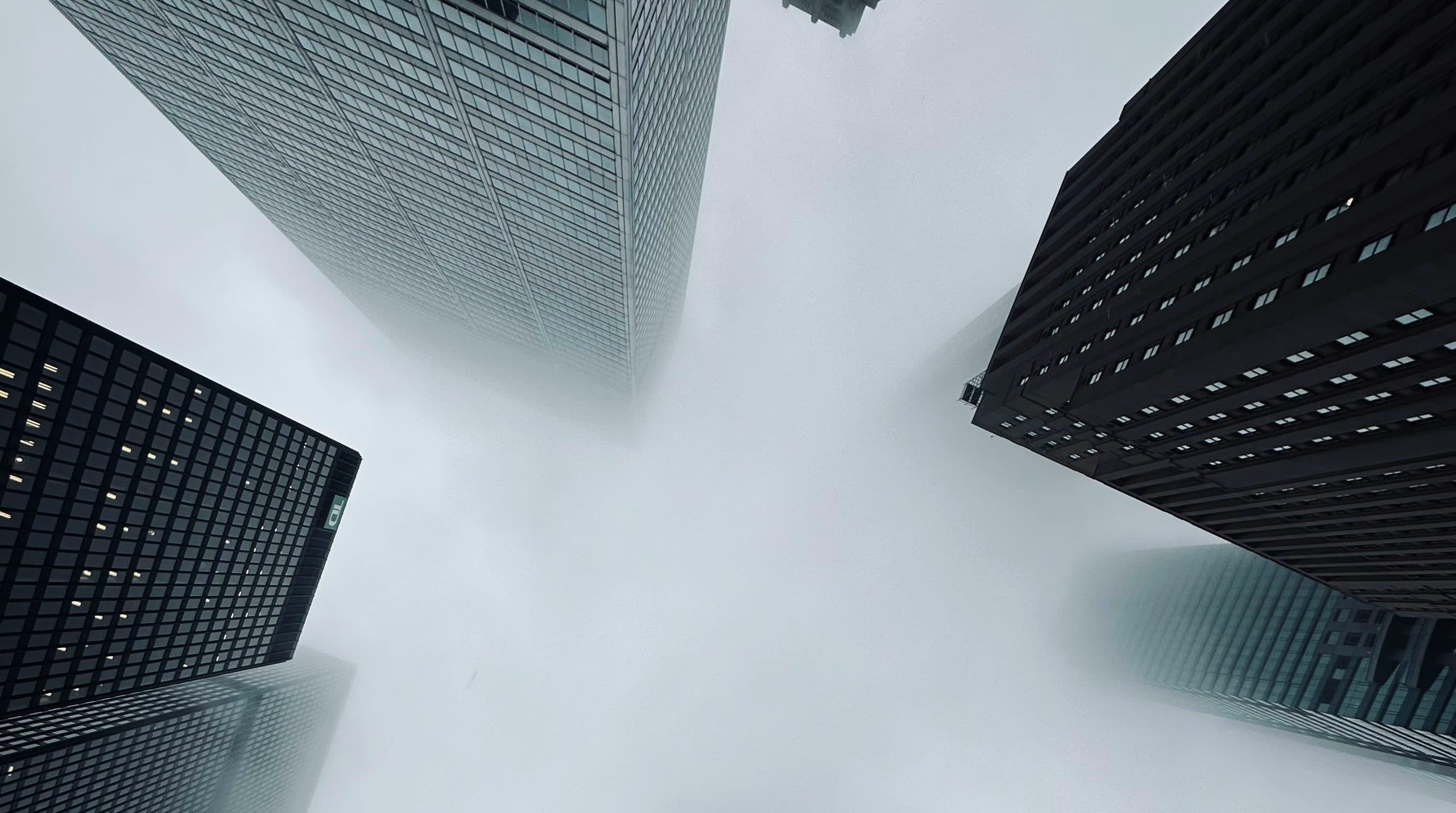 Office towers seen from below, their tops lost in fog