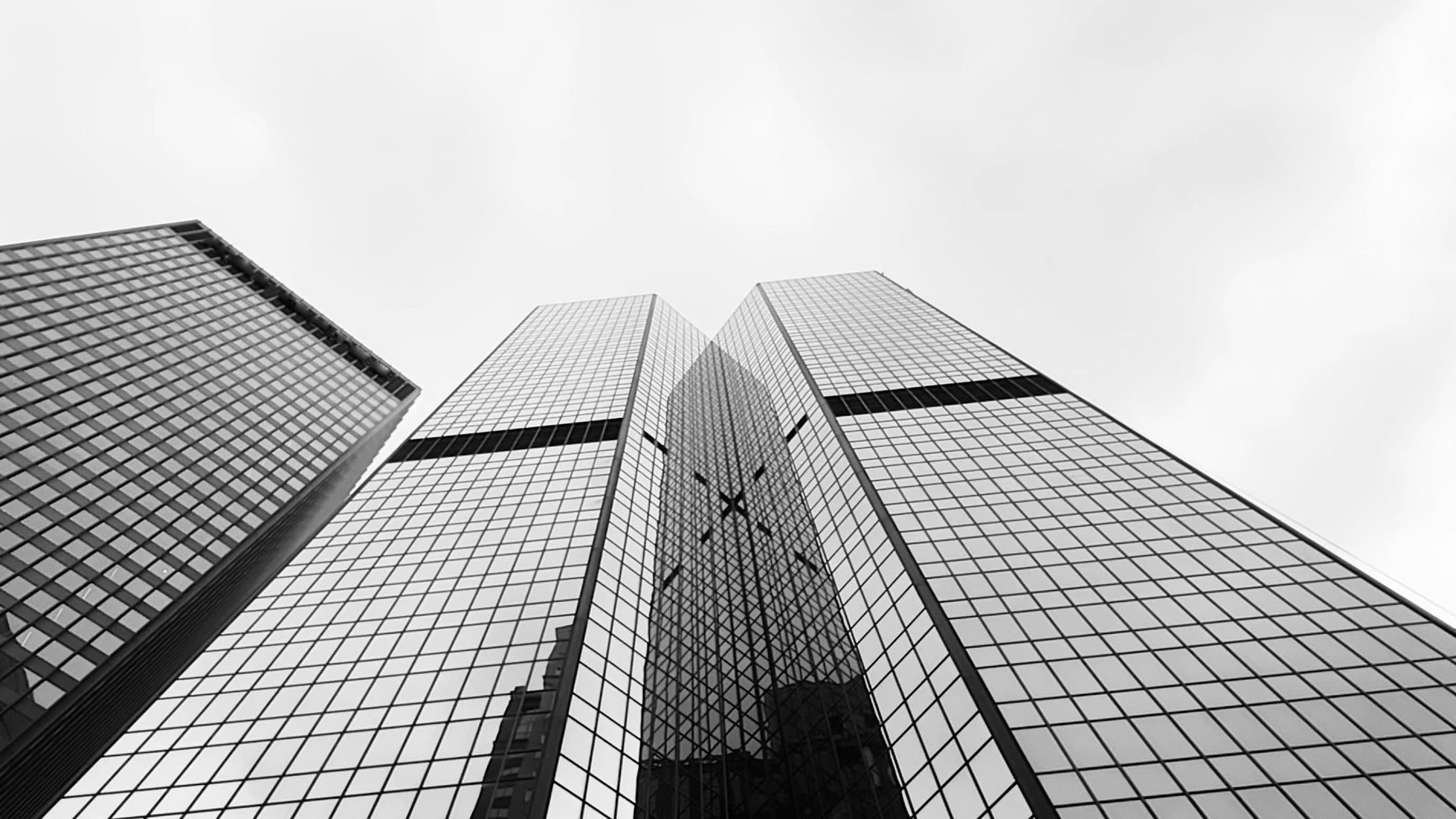Twin glass towers seen from below against a grey sky